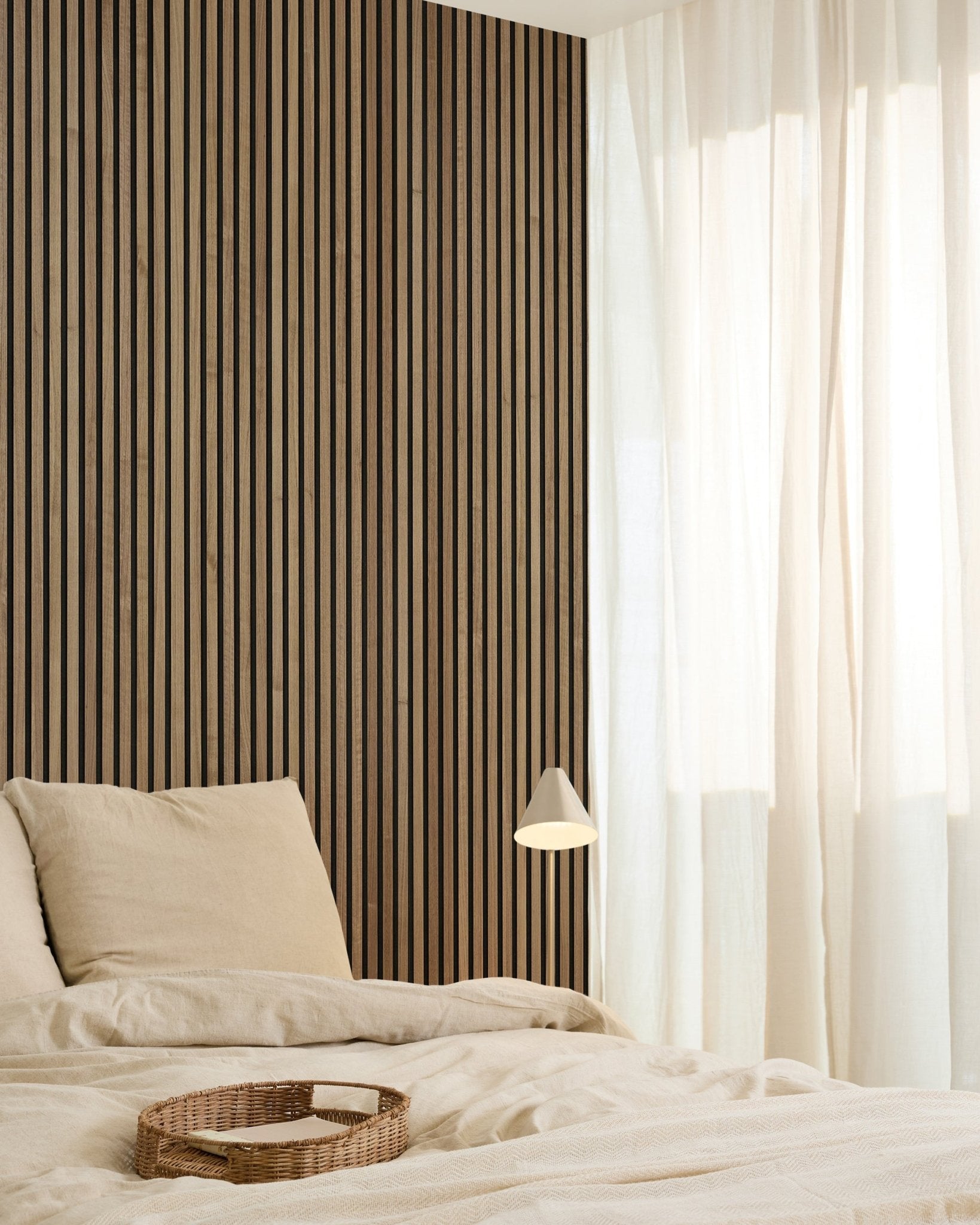 Camera da letto minimalista con un WoodUpp Original Akupanel Walnut Pannello acustico (240x60 cm) sulla parete, biancheria da letto beige, tende leggere, vassoio intrecciato e lampada da parete small.
